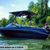 black boat sitting on the lake with lots of green trees around it. Showcasing the Big Air X tower and Super Shadow Bimini with a young man sitting in the back of the boat.