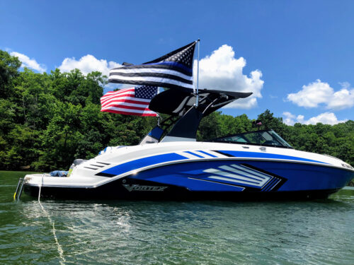 blue and white 2019 Vortex 2430vrx boat sitting on the water with 2 flags waving behind the boat tower