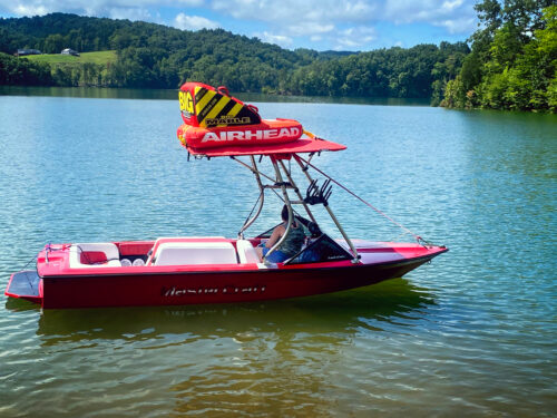 red mastercraft boat on the water with the big air tube top bimini carrying a tube on top