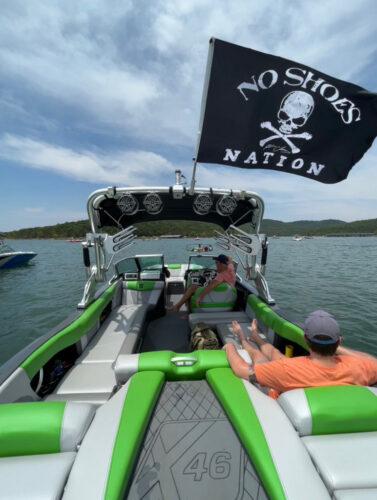 Rear view of a boat showing lots of speakers and a black flag with a skull and crossbones that reads "No shoes Nation"