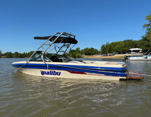 White and blue Malibu boat showcasing the Big Air Cuda tower mounted by the bow and sweeping towards the stern. The tower has the Big Air Collapsible Bimini mounted onto it too.