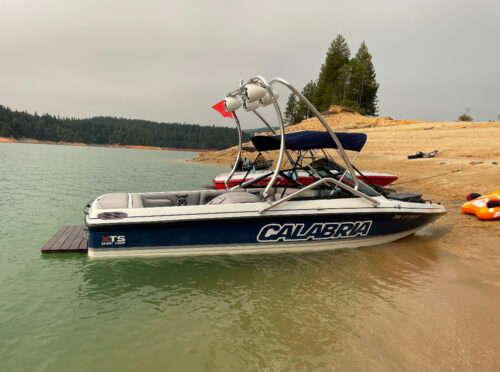 A blue and white Calabria sport comp boat beached in the water showing it has a Big Air Haus tower mounted on it.