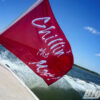Red Flag with white text saying "Chillin the Most" mounted at the back of a boat, going across the water.