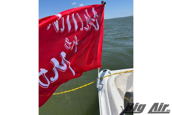 Red Flag with white text saying "Chillin the Most" mounted at the back of a boat, going across the water.