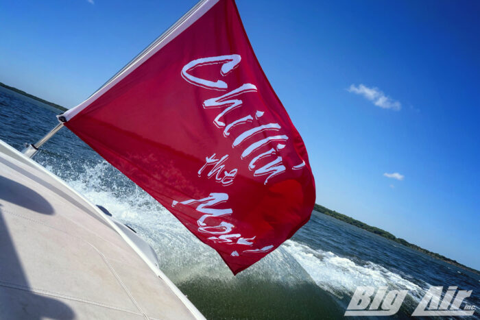 Red Flag with white text saying "Chillin the Most" mounted at the back of a boat, going across the water.